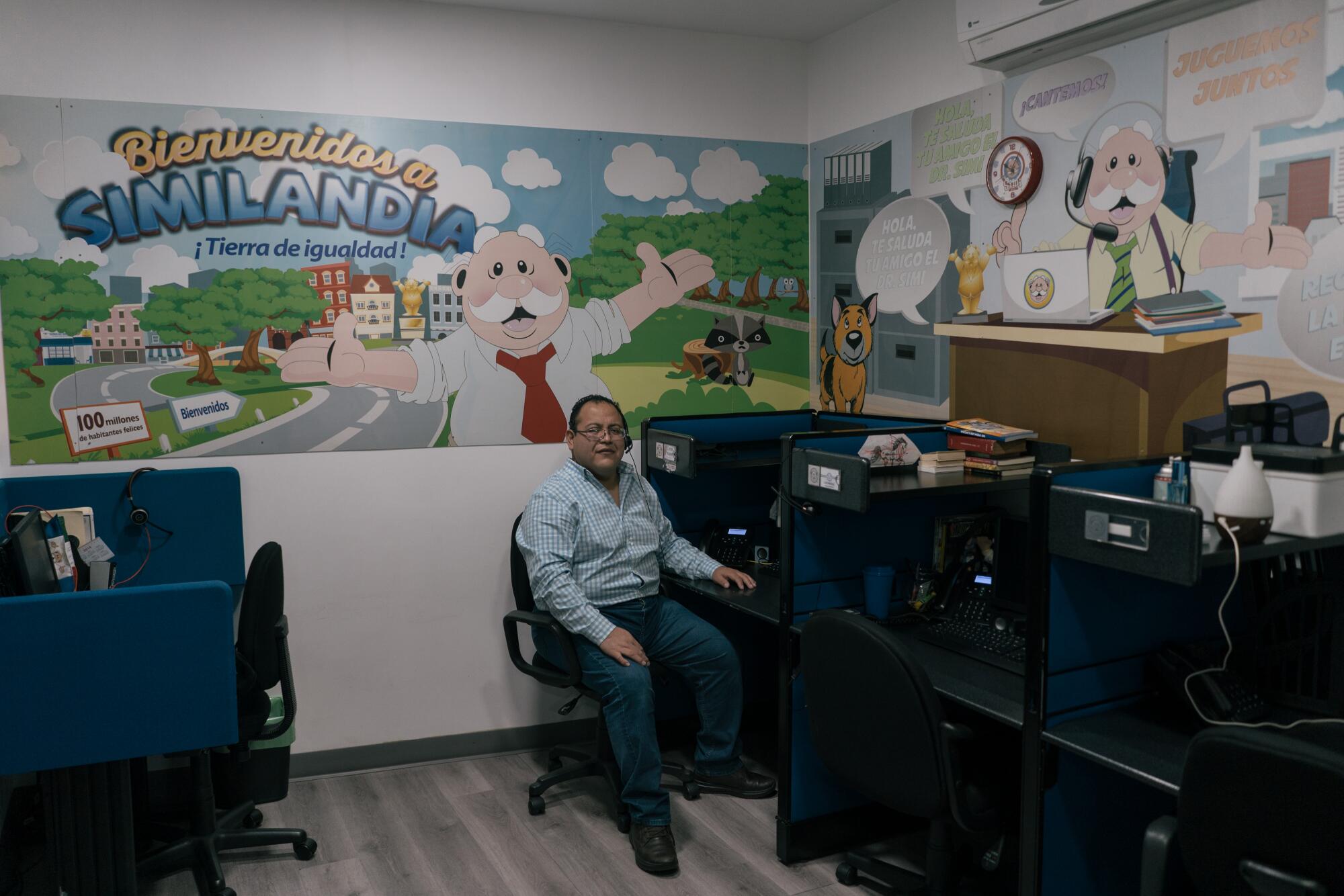 A man sits at a workstation. Behind him is a poster of a mustachioed character and the words Bienvenidos a Similandia 