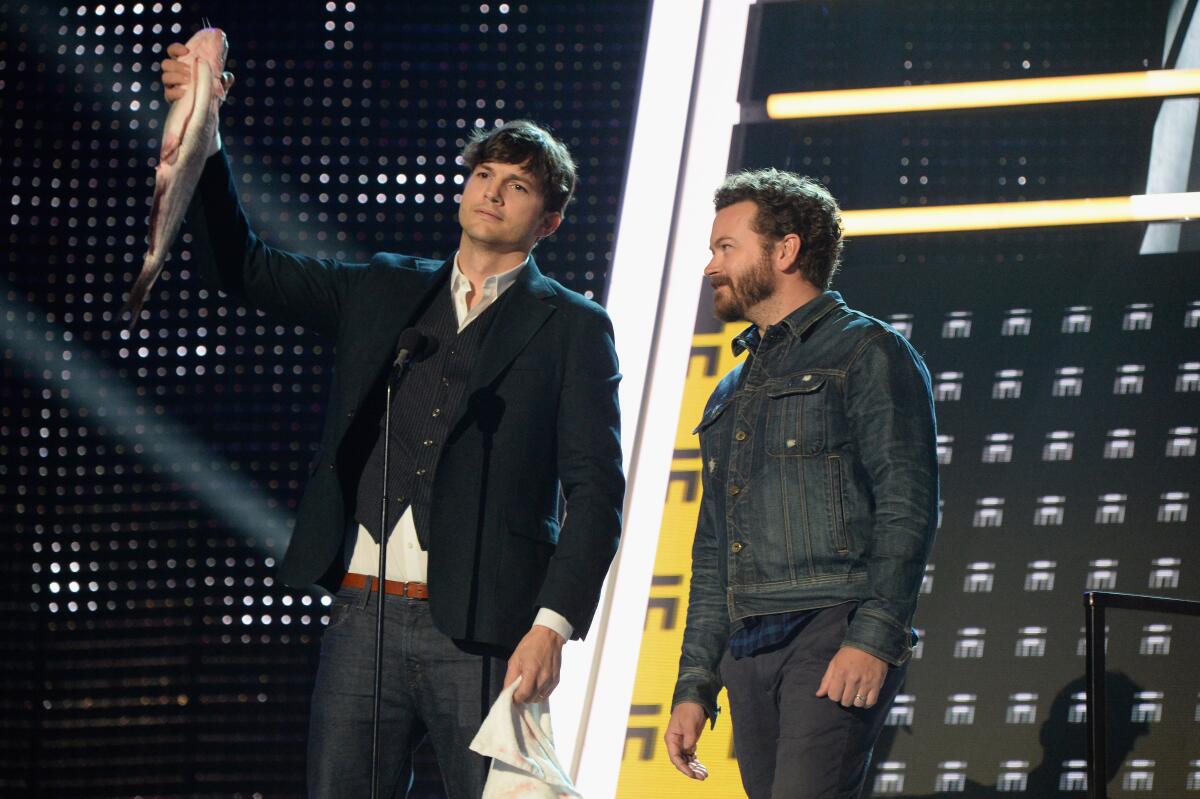 Ashton Kutcher holds up a fish while standing on an awards stage next to Danny Masterson.