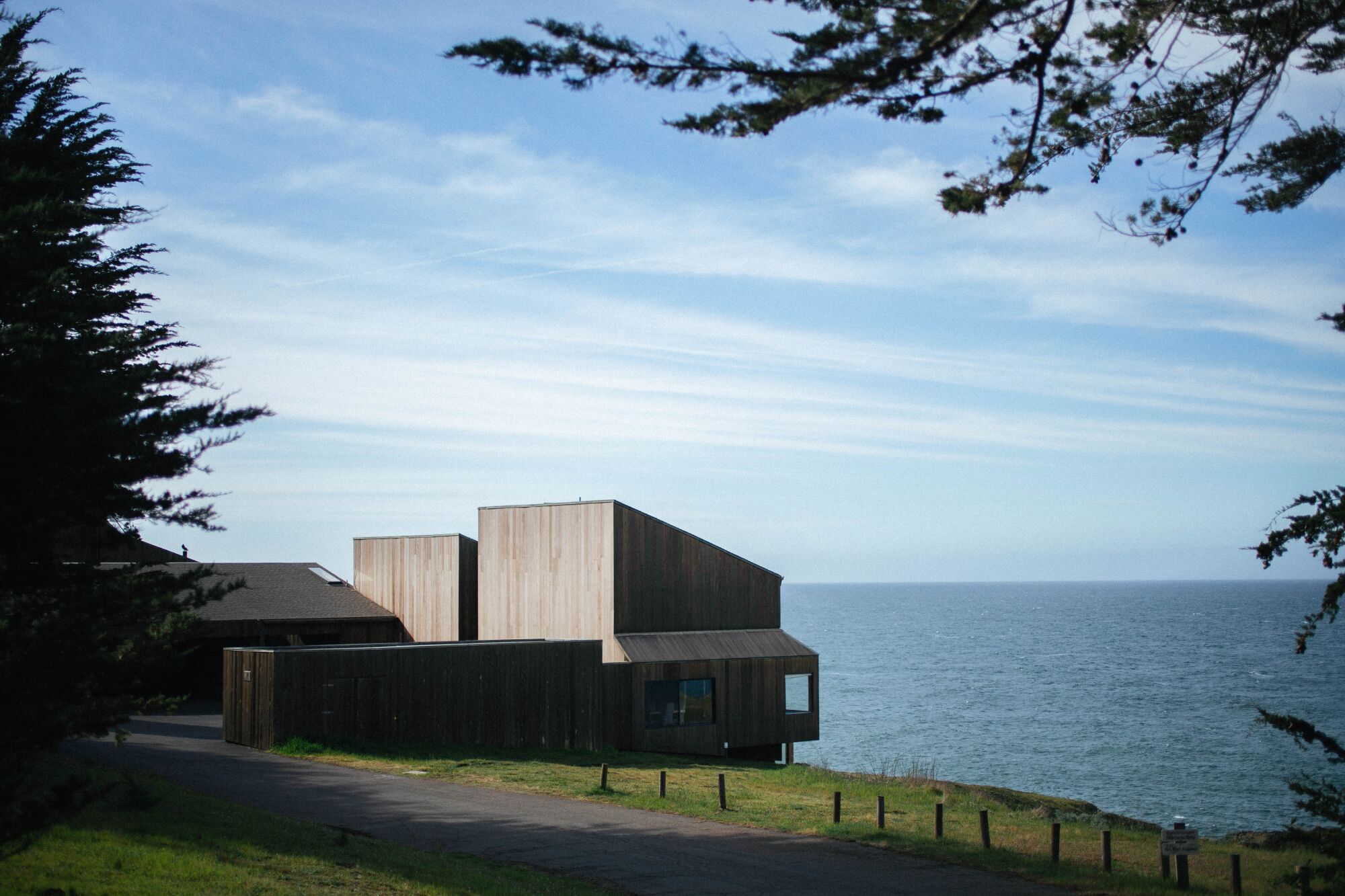 A boxy wooden building sits on a bluff overlooking the ocean.