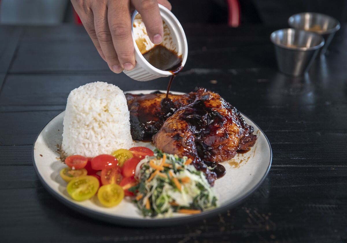 AC Boral pours sauce over a plate of Dad’s glazed BBQ chicken at Bebot Filipino Soul Food in Long Beach