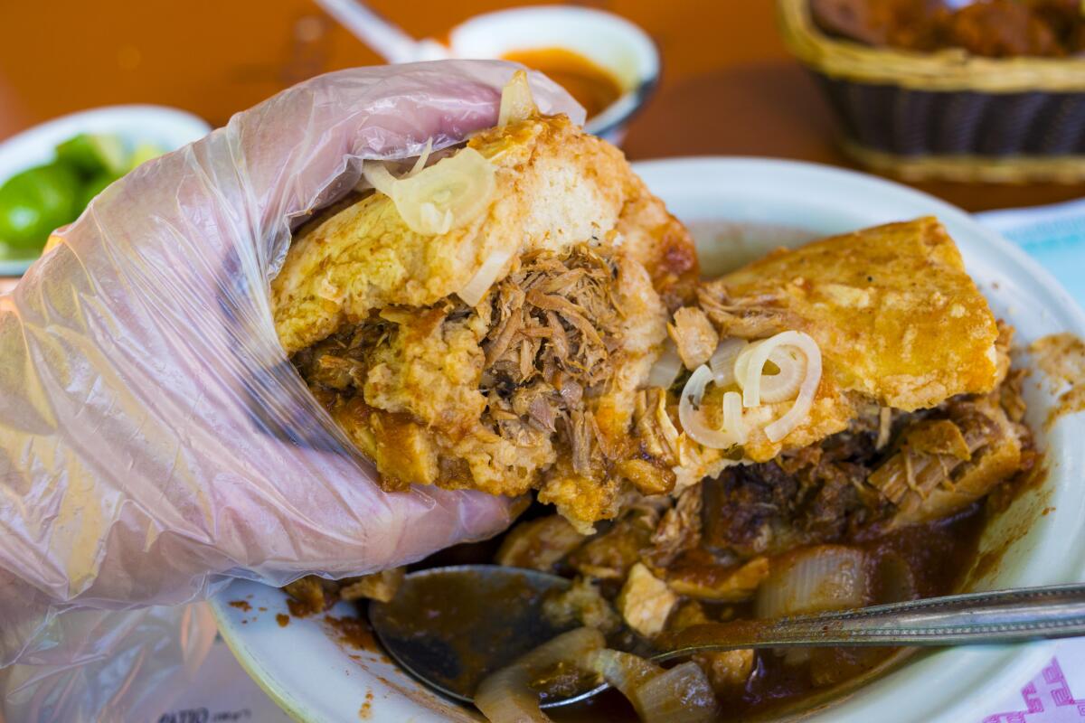A hand wearing a plastic glove holds up a hunk of torta ahogada.