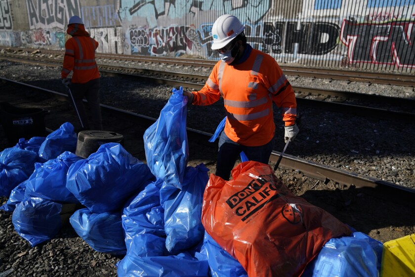 Workers bag cardboard and other discarded items at a Union Pacific railroad site on Thursday, Jan. 20, 2022, in Los Angeles. Gov. Gavin Newsom on Thursday promised statewide coordination in going after thieves who have been raiding cargo containers aboard trains nearing downtown Los Angeles for months, leaving the tracks blanketed with discarded boxes. (AP Photo/Ashley Landis)