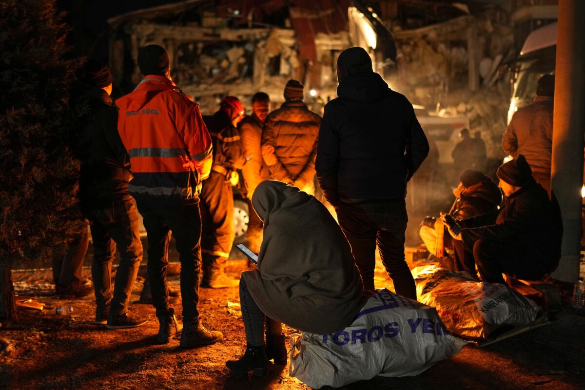 A family get warm with a fire in front of their destroyed home as rescue teams search for people in Elbistan, southern Turkey, Wednesday, Feb. 8, 2023. With the hope of finding survivors fading, stretched rescue teams in Turkey and Syria searched Wednesday for signs of life in the rubble of thousands of buildings toppled by a catastrophic earthquake. (AP Photo/Francisco Seco)
