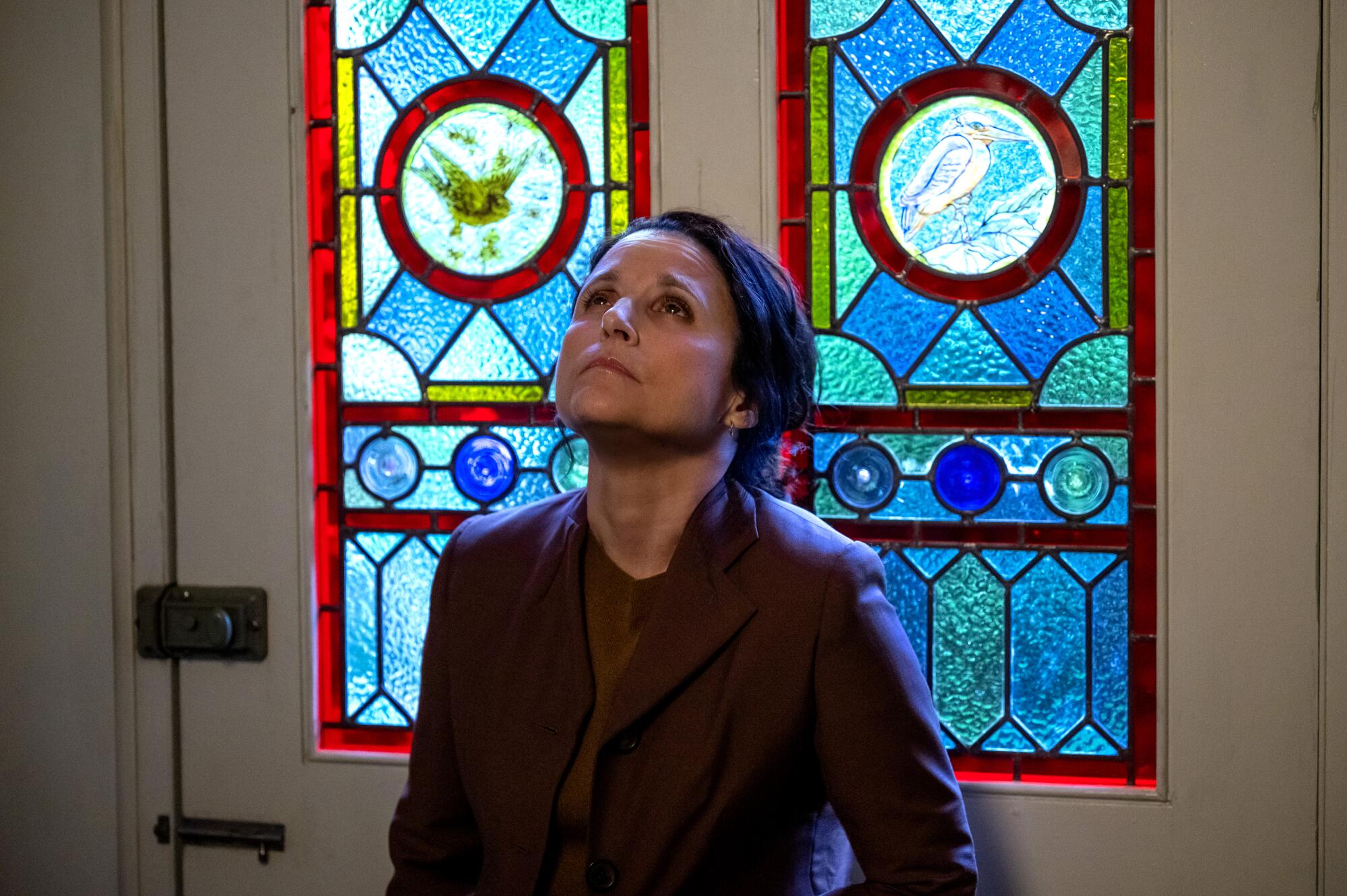 A grieving woman stares upward, a stained-glass window behind her