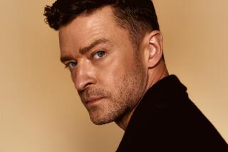 Justin Timberlake in black looks over his left shoulder as he poste against a solid light yellow backdrop