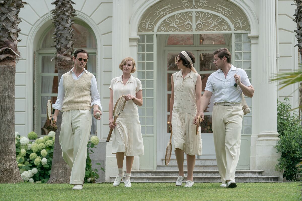 Two men and two women wearing white clothes and carrying wooden tennis rackets.