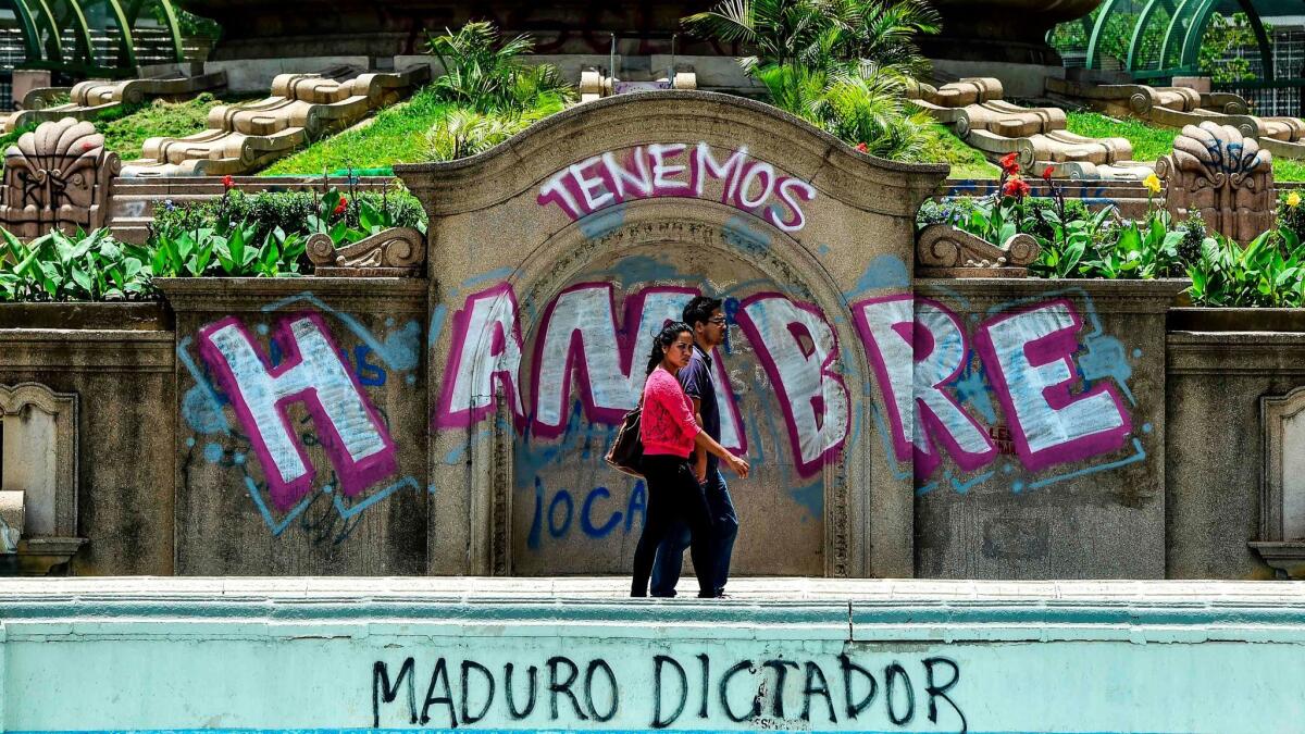 A couple walks past graffiti reading, "We are hungry," and, "Maduro dictator," in Caracas on Aug. 8, 2017.