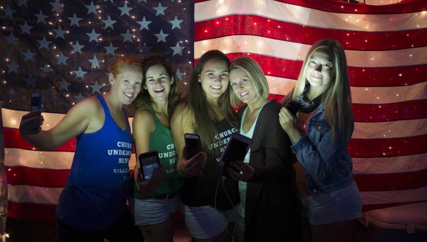 Country music fans Debbie Clark, of Fullerton, left, Kitty Borchard, of Costa Mesa, Caitlin Roberto, of Norwalk, Jenny Stevens, of Downey, and Nicole Ray, of Anaheim, pose with their phones by an illuminated American flag hanging on their RV at dusk in the RV Resort for the 10th anniversary of the Stagecoach Country Music Festival.
