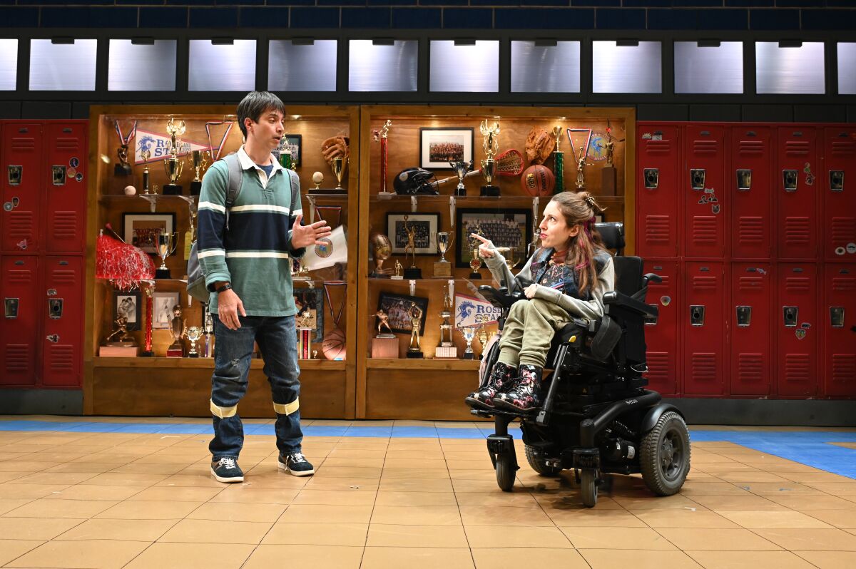 A boy stands talking to a girl in a wheelchair in a high school hallway 