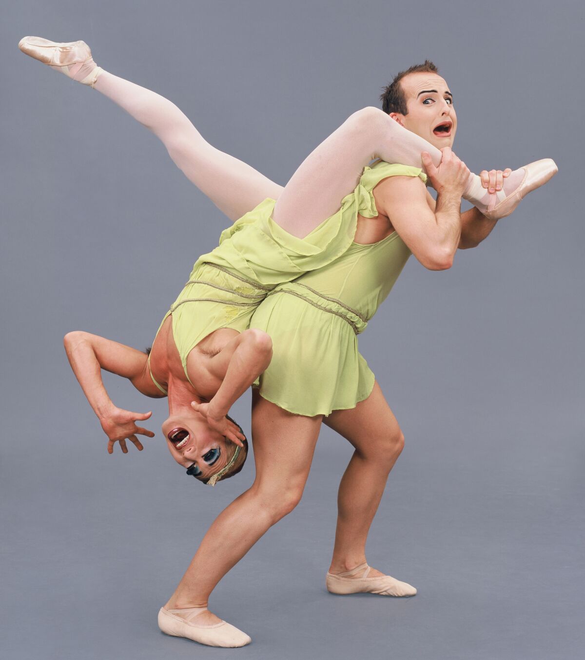 One male ballet dancer carries another by the leg over his shoulder