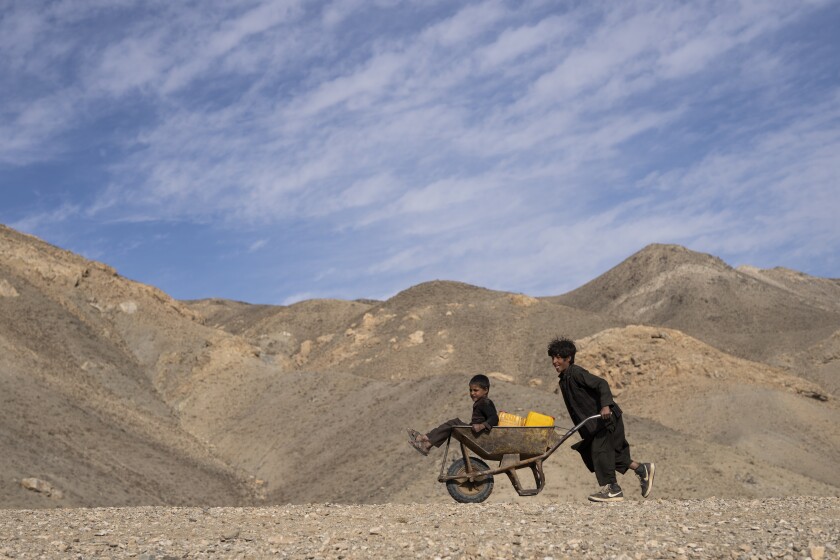 A boy pushes a wheelbarrow with canisters and his younger brother, on their way to collect water from a stagnant pool, about 3 kilometers (2 miles) from their home in Kamar Kalagh village outside Herat, Afghanistan, Friday, Nov. 26, 2021. Afghanistan's drought, its worst in decades, is now entering its second year, exacerbated by climate change. (AP Photo/Petros Giannakouris)