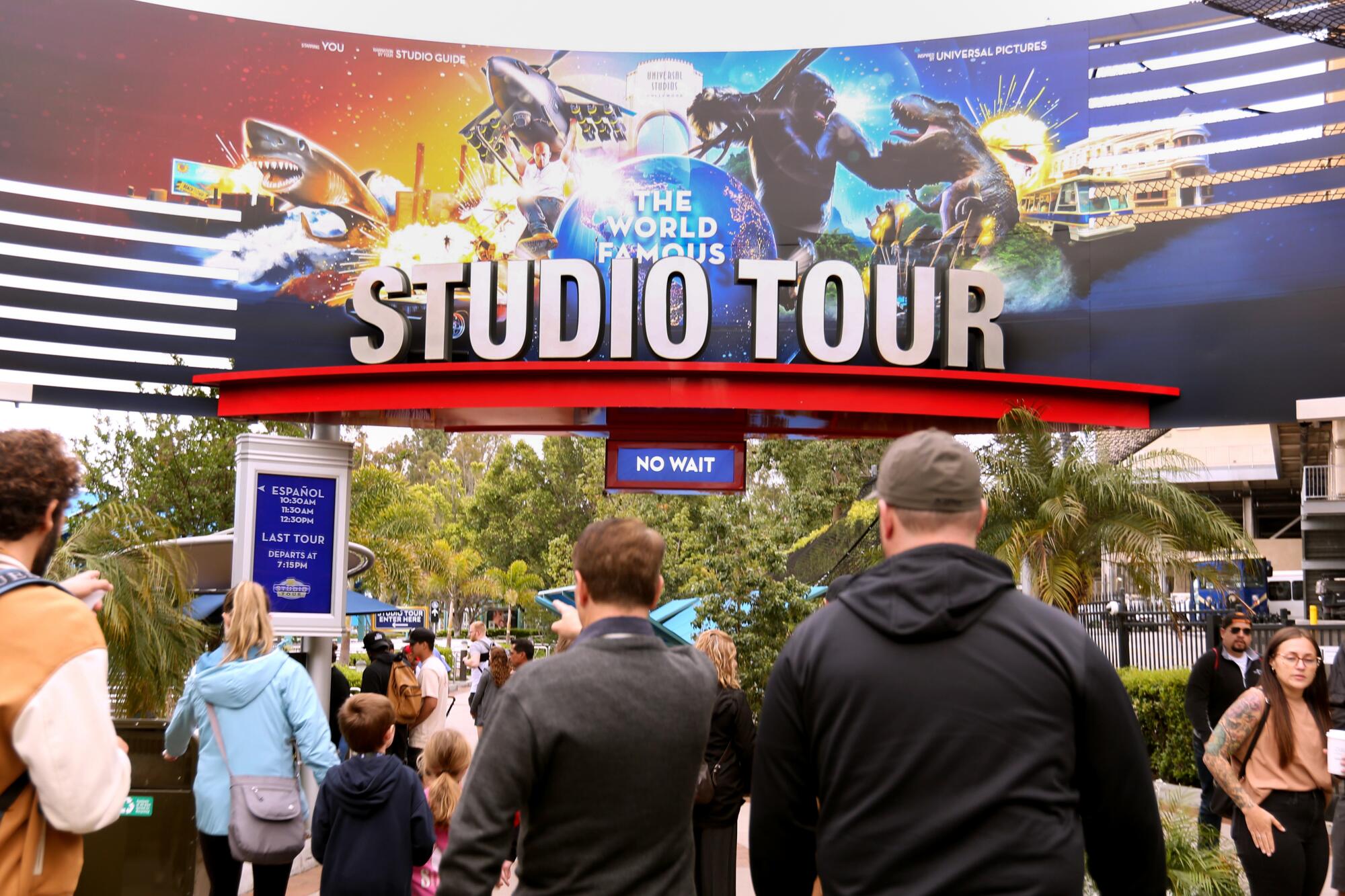 People walk toward an entrance gate with a photo collage and the words "Studio Tour."