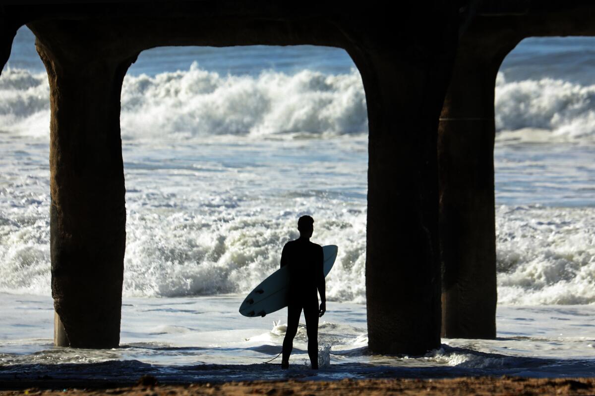 A surfer stands under a pier at a beach