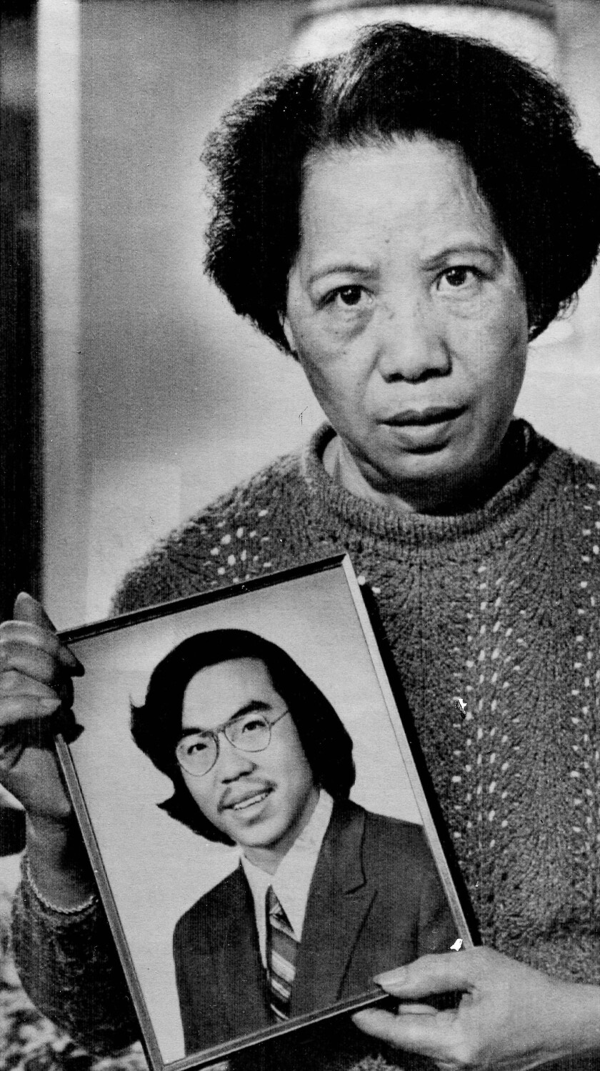 A black and white photo of a middle-aged Asian woman holding a framed picture of a younger Asian man
