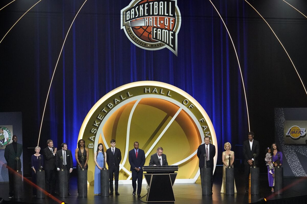 People in formalwear stand on a stage where a sign reads "Basketball Hall of Fame."