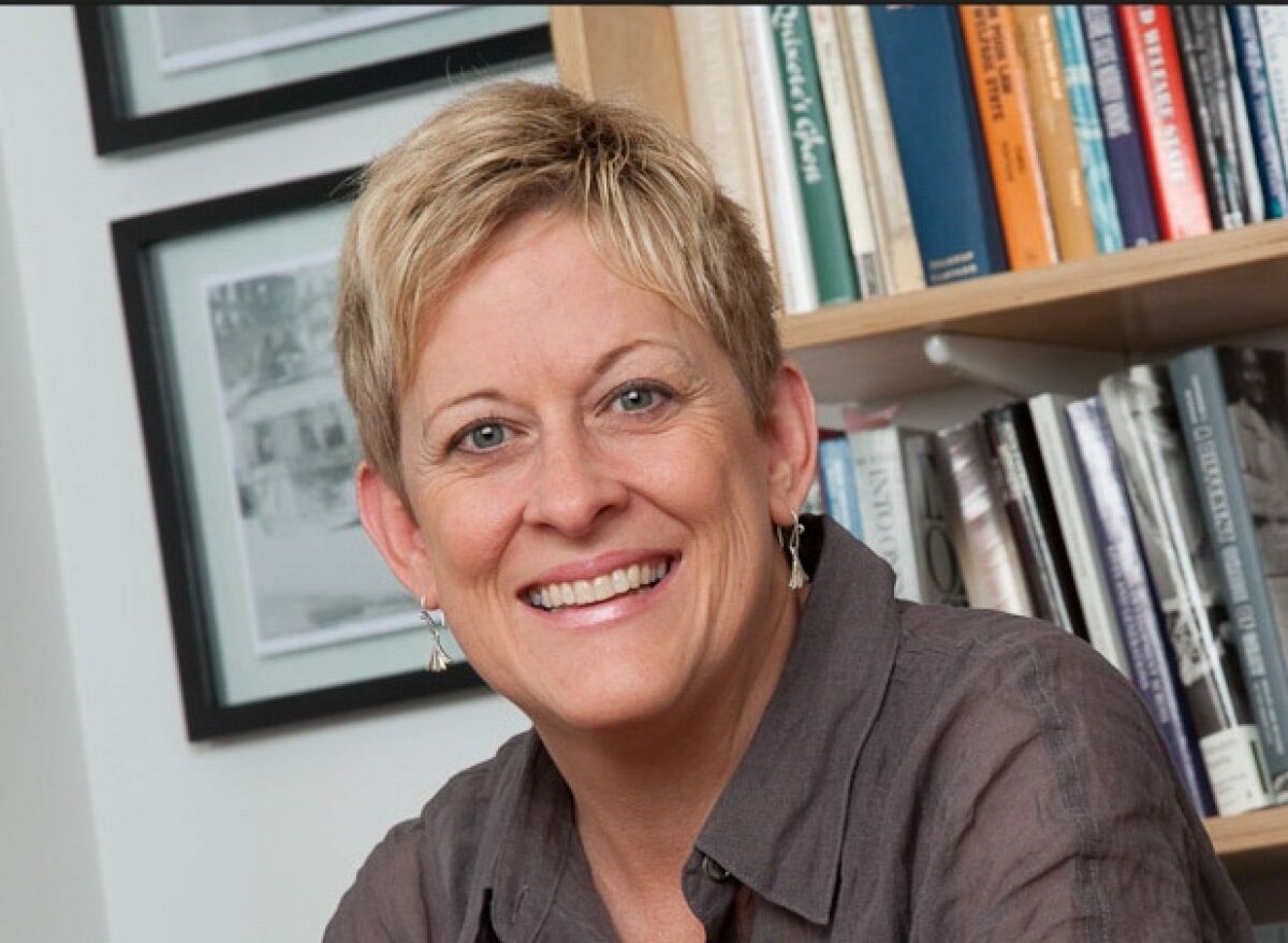 A woman with short blond hair smiling in front of a bookcase.