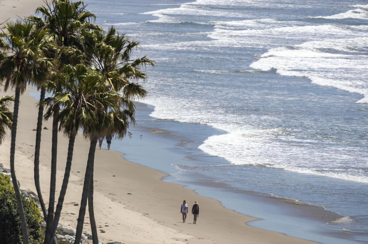 A couple walk on Broad Beach in Malibu