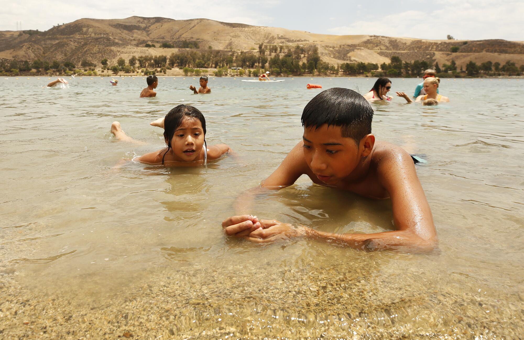 Samuel Garcia, 12, collects shells in the sand for his sister Paola Garcia, 4, at Castaic Lake Lagoon