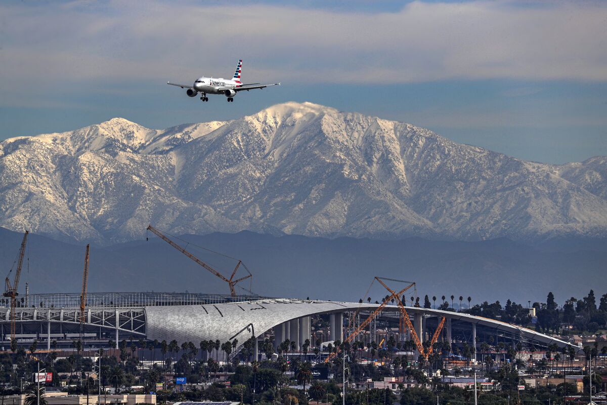 A plane approaches Los Angeles International Airport on Saturday against the backdrop of snow-covered mountains and over SoFi Stadium, which will be the new home of the Los Angeles Rams and Chargers when it opens next summer.