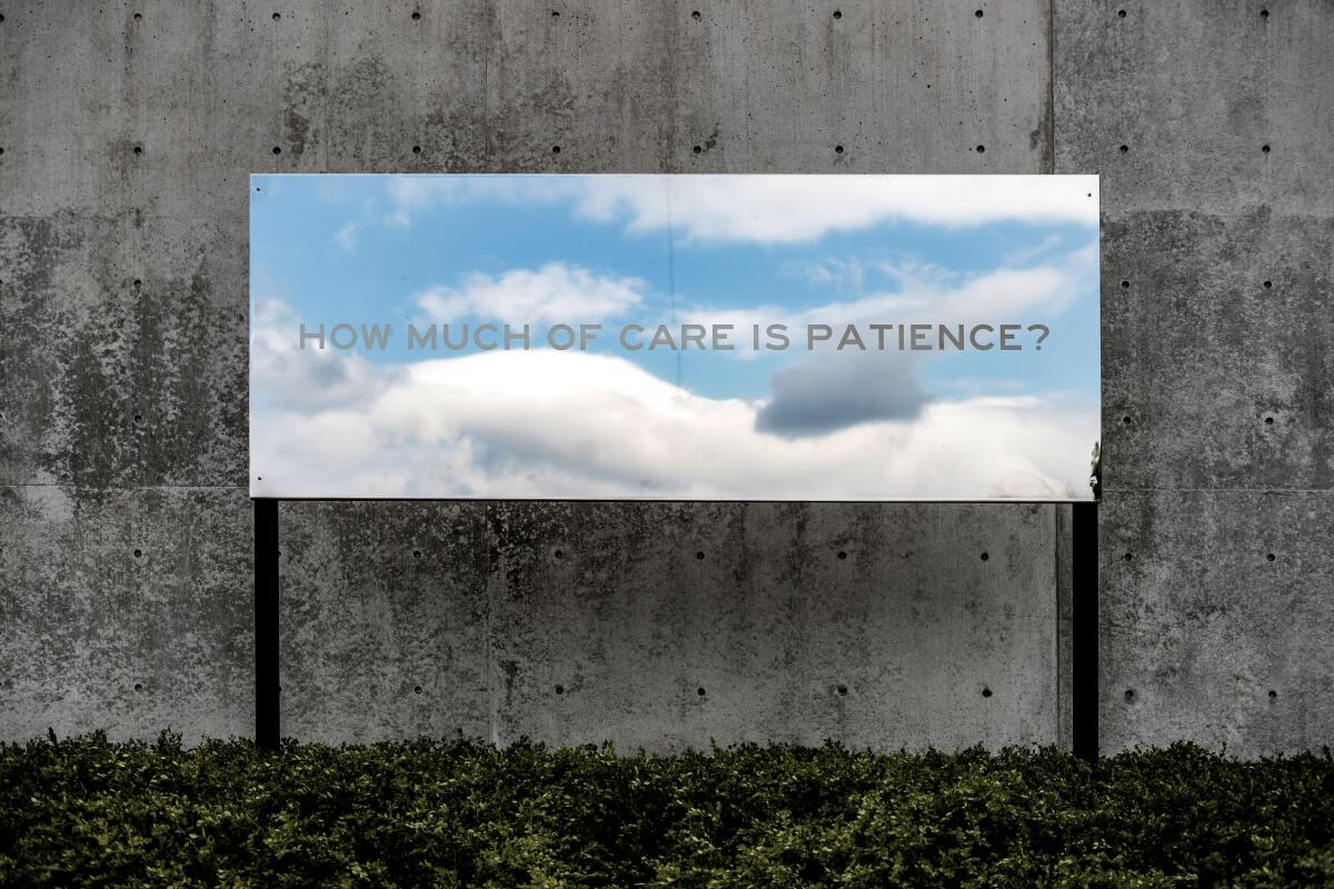 A billboard of sky and clouds against a concrete wall. It reads, "How much of care is patience?"