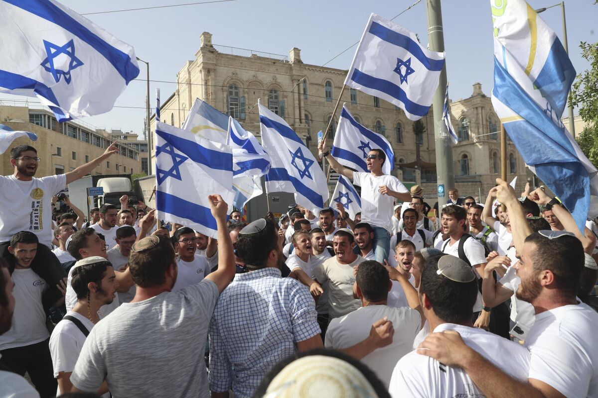 Men yell and crowd together, holding up Israeli flags.