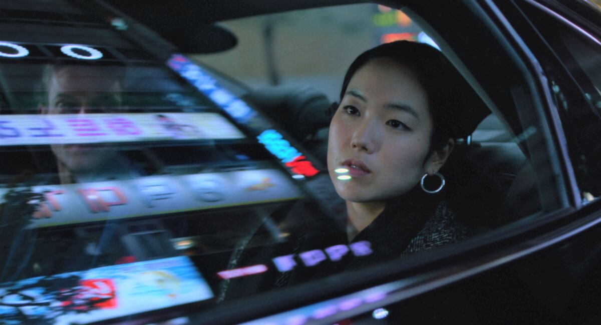A woman in a car with neon signs reflecting in the window in the movie "Return to Seoul."