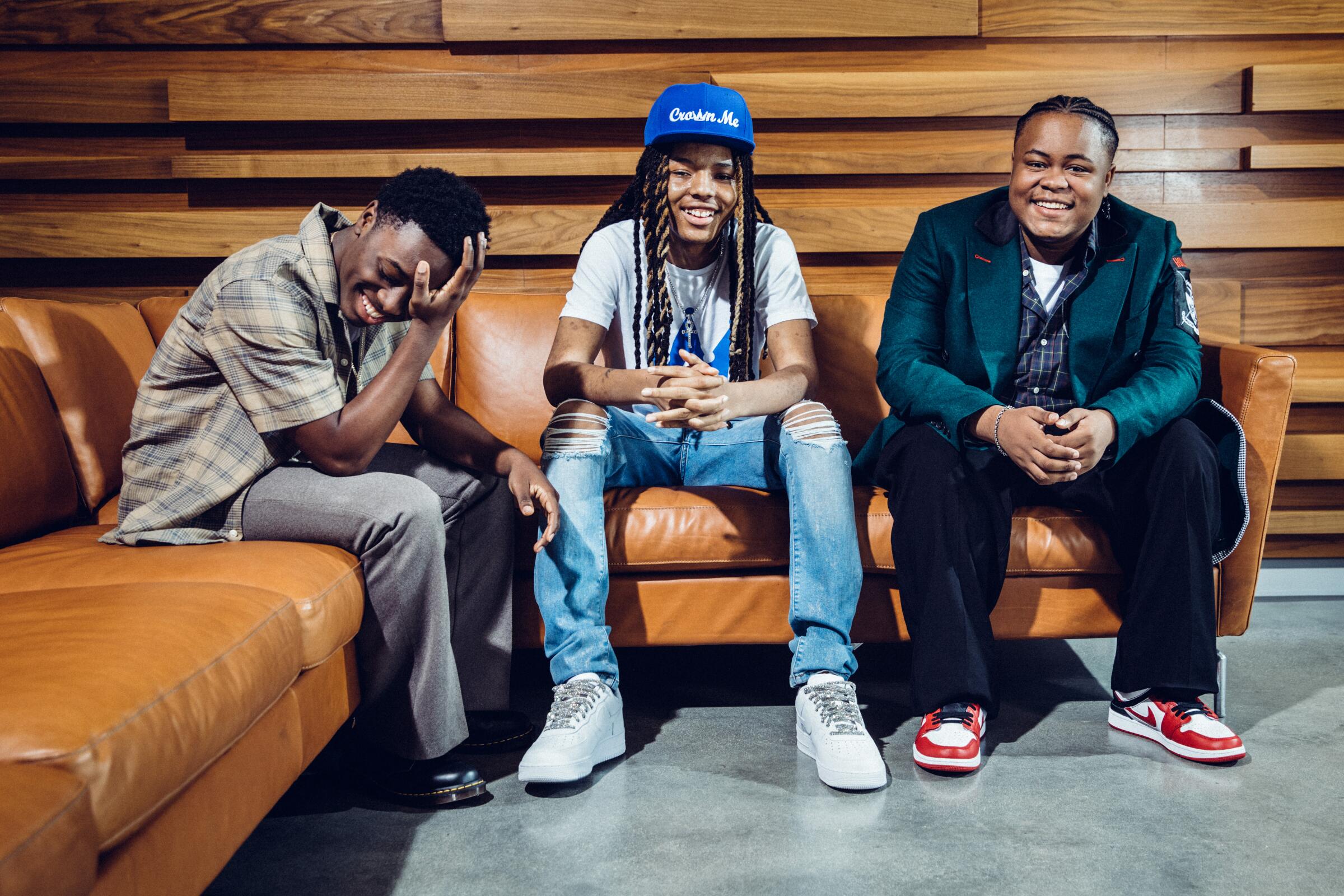 Three teenage actors sitting on a tan leather couch smiling