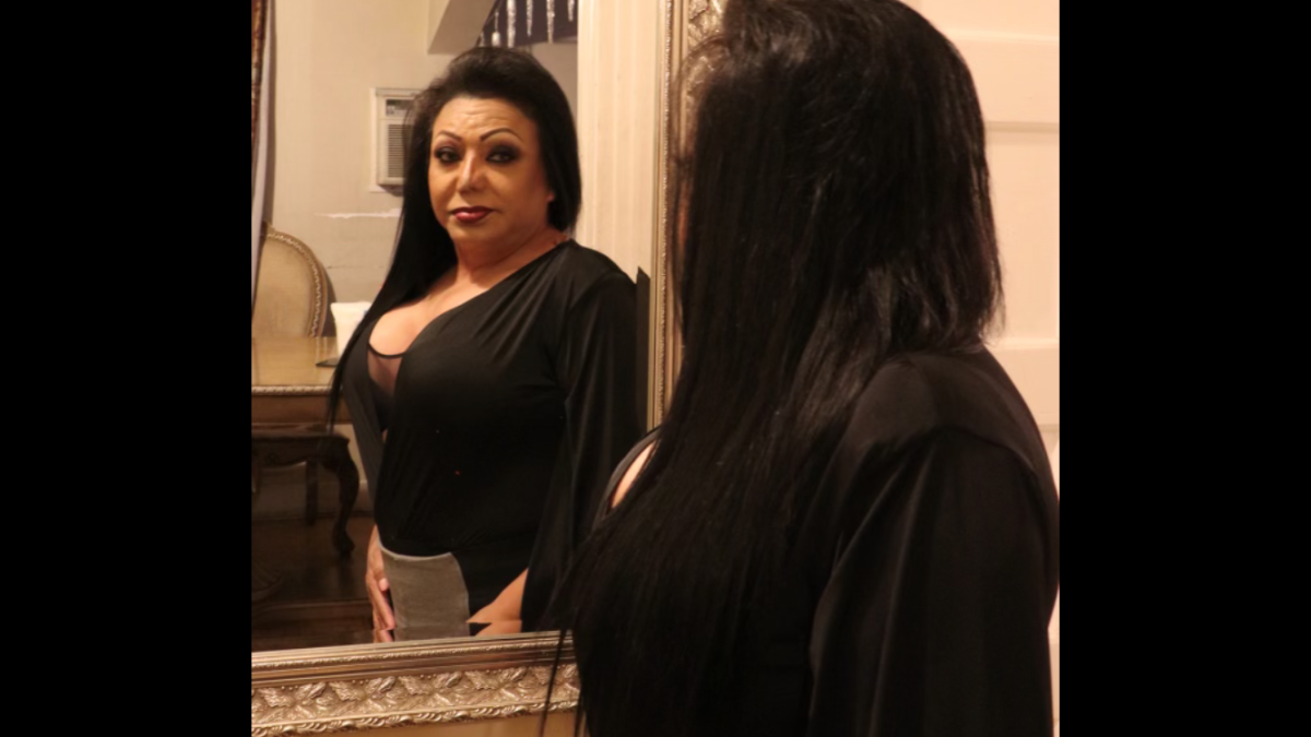 A woman looks in a mirror with her hands by her side