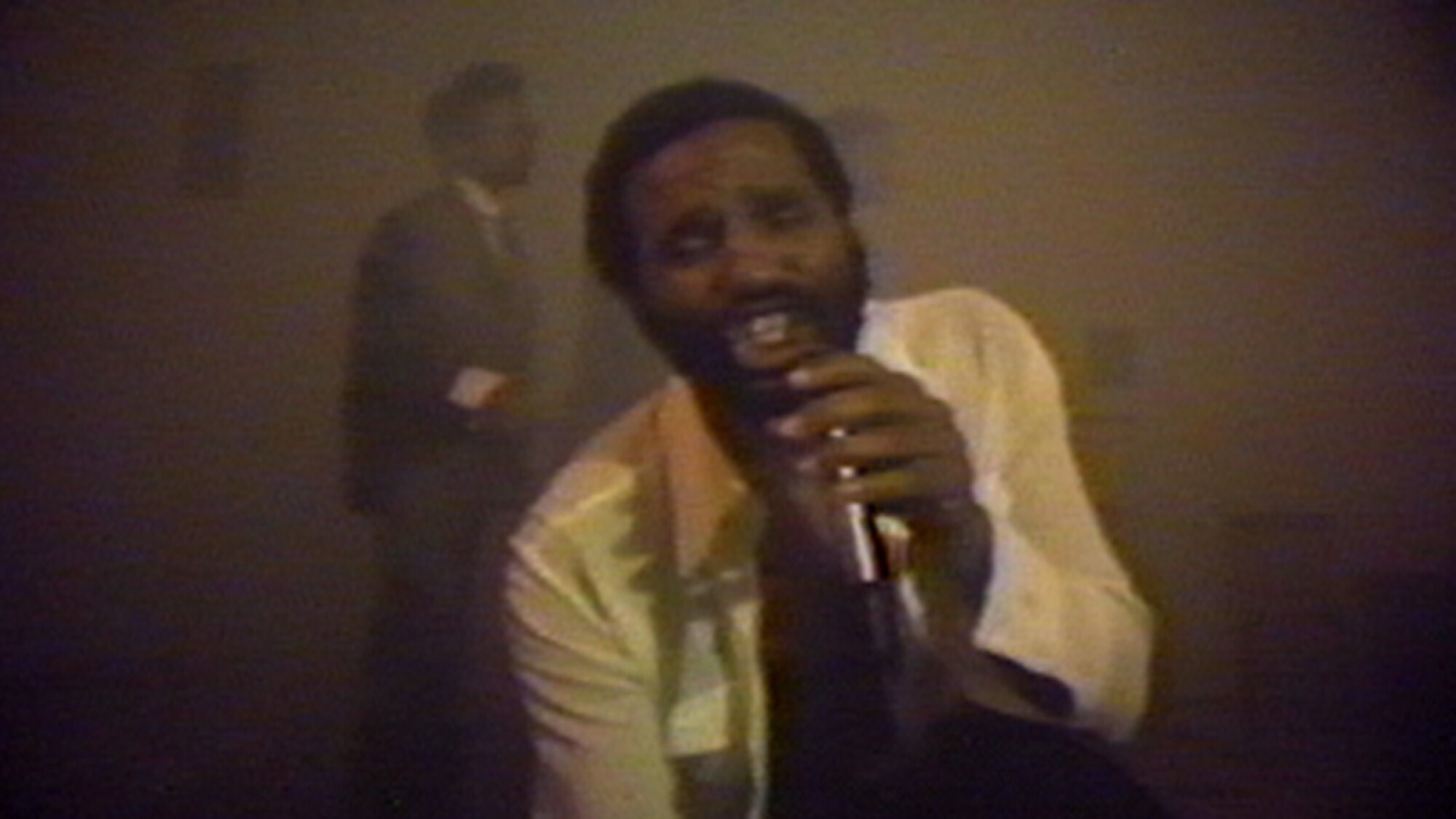 A video still shows Ulysses Jenkins singing dramatically into a microphone as a trio performs behind him