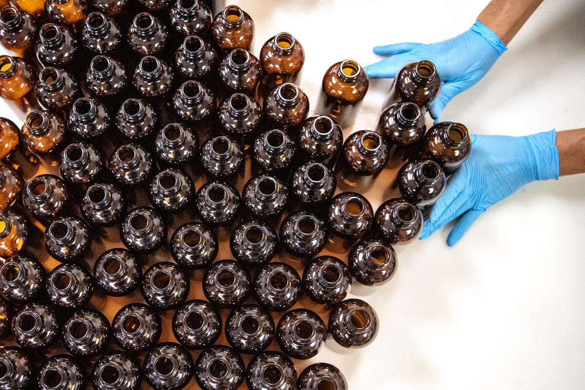 Gloved hands push a mass of empty brown glass bottles on a table.