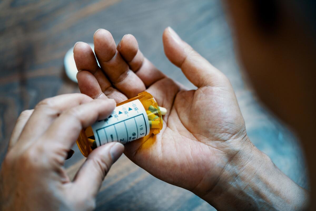 Close-up of a male hand holding a pill bottle pouring medication into his hand in his house