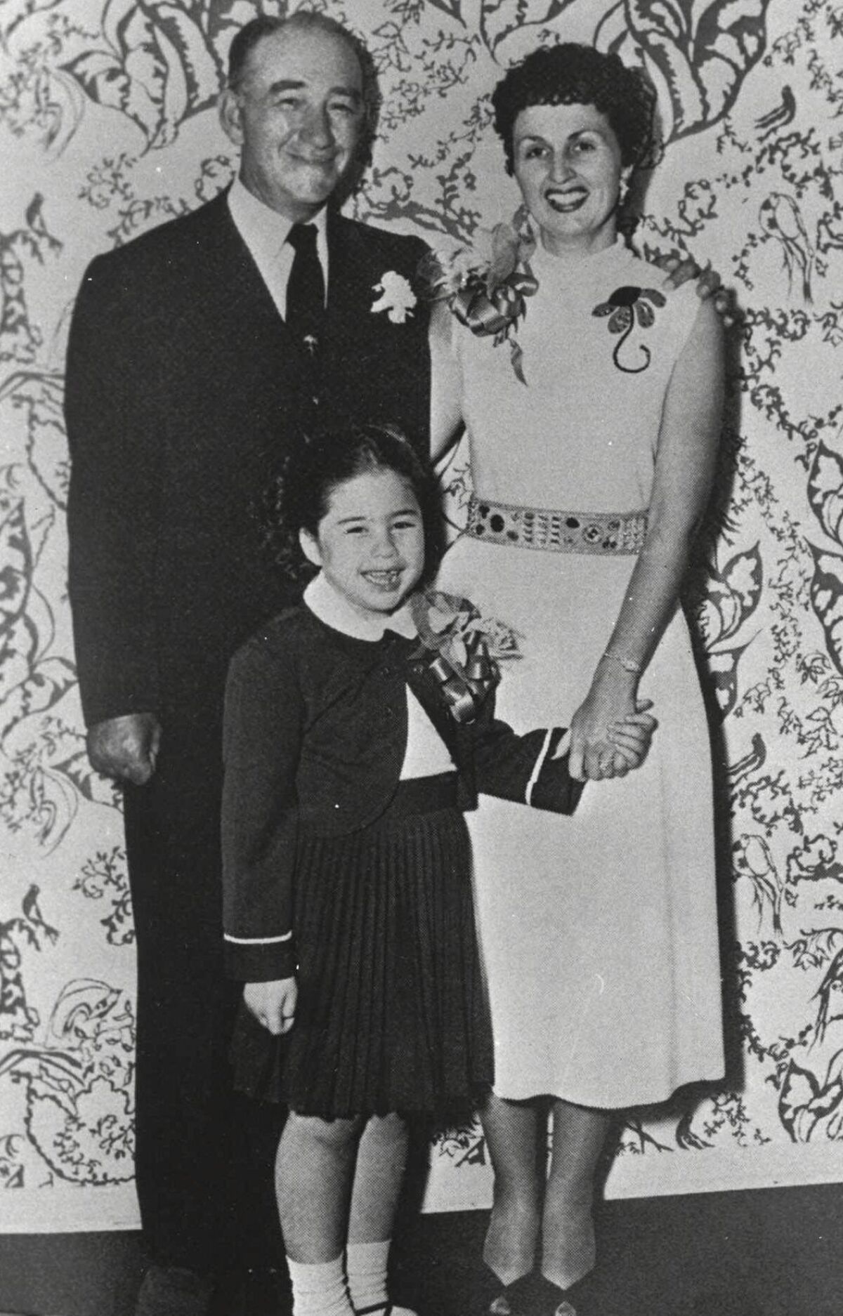 A child stand in between her parents, holding her mother's hand.