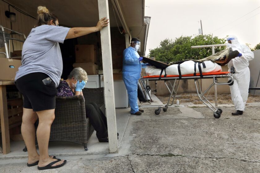 MC ALLEN, TEXAS-July 28, 2020-Maura Ramirez, 41, (right) watches as Juan Lopez (center) and Elizondo Flores, 48, remove the body of her mother Amalia Tinoco, 92, from her home in Pharr, Texas, earlier this month after she died of COVID. In the Rio Grande Valley towns of McAllen and Mission, Texas, Juan Lopez works collecting the bodies of people who have died from COVID-19. (Carolyn Cole/Los Angeles Times)