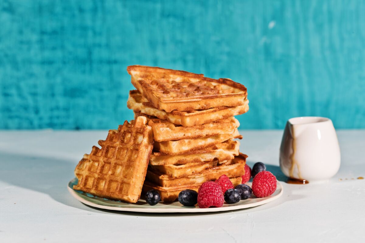 A stack of golden waffles, cut into triangles, on a plate with raspberries and blueberries, with maple syrup.