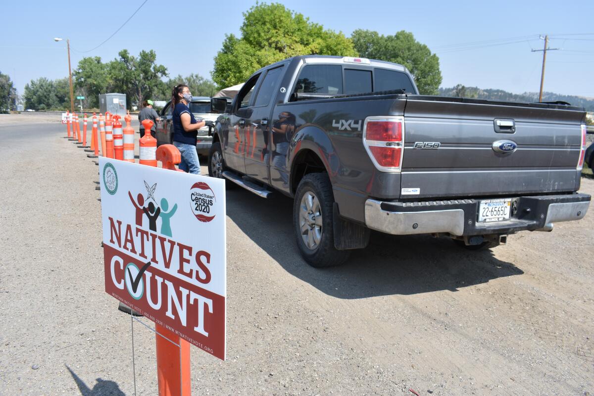 A census worker talks to a driver next to a Census 2020: Natives Count sign