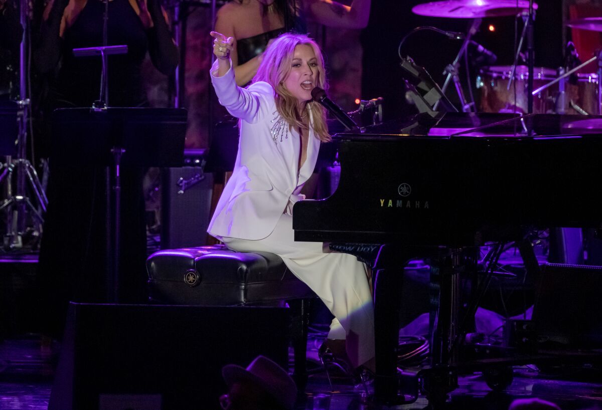 Una mujer con traje blanco canta y toca el piano.