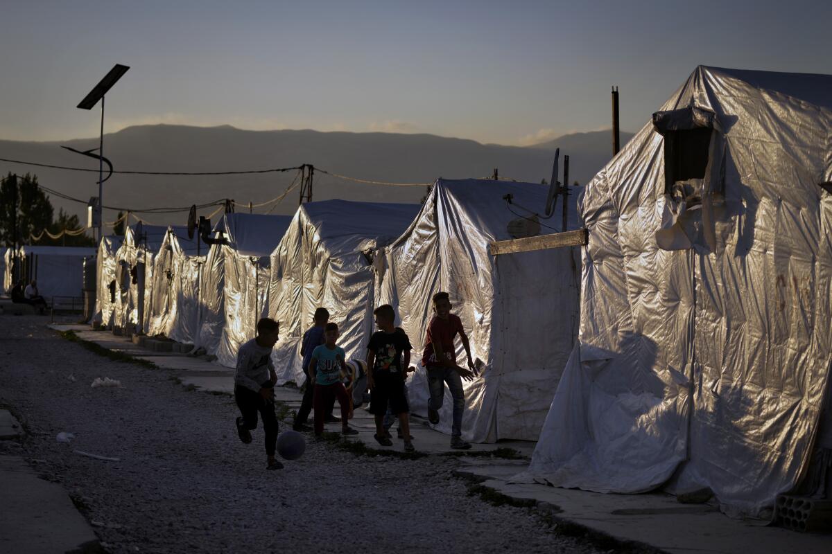 Syrian children play soccer in front of a row of tents.