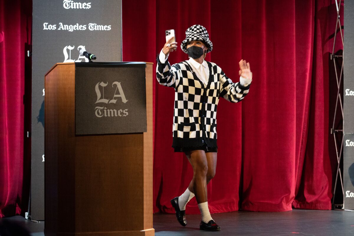 Janelle Monáe walks onstage waving and holding up her phone.
