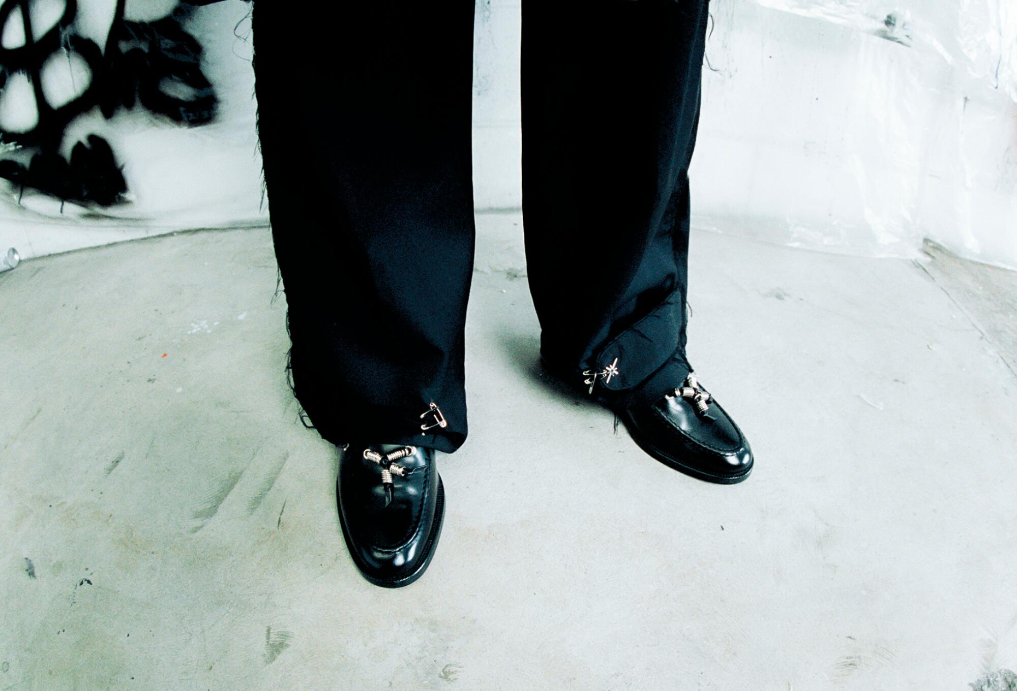 A person's lower legs clad in black pants with black shoes.