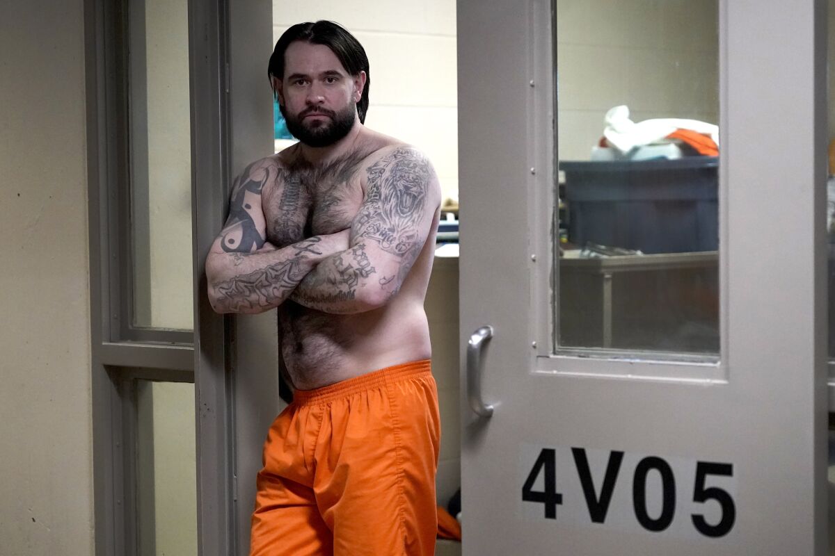 Erik Eck, a former member of the Latin Kings gang stands in the doorway of his cell at the DuPage County, Ill., Jail displaying tattoos that symbolize his status with the gang, Thursday, Feb. 3, 2022, in Wheaton, Ill. Under penalty of a beating or death, Eck pledged when he joined the Latin Kings in Chicago at 13 to adhere to the gang's first rule: "Once a King, always a King." Tattoos that cover his entire body express fealty forever to the gang, one of the nation's largest. (AP Photo/Charles Rex Arbogast)