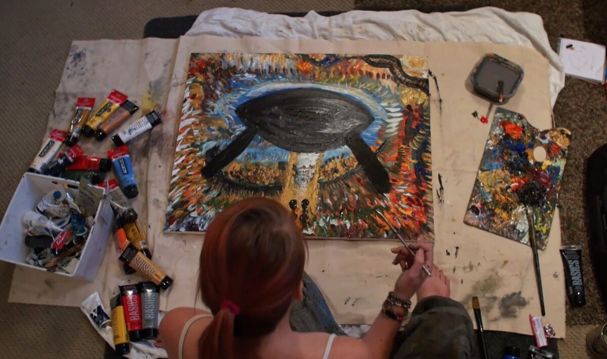 A person paints on a canvas on the table in front of them.