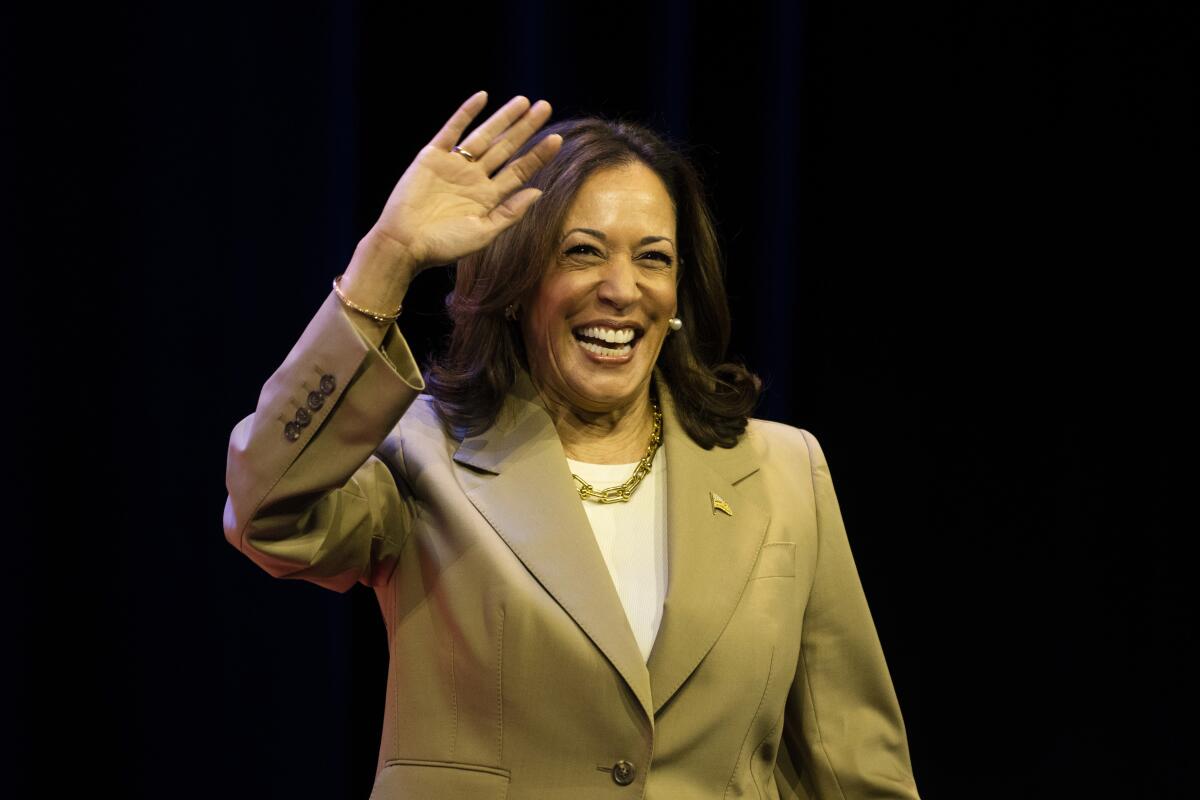 Vice President Kamala Harris smiles and waves against a black background.