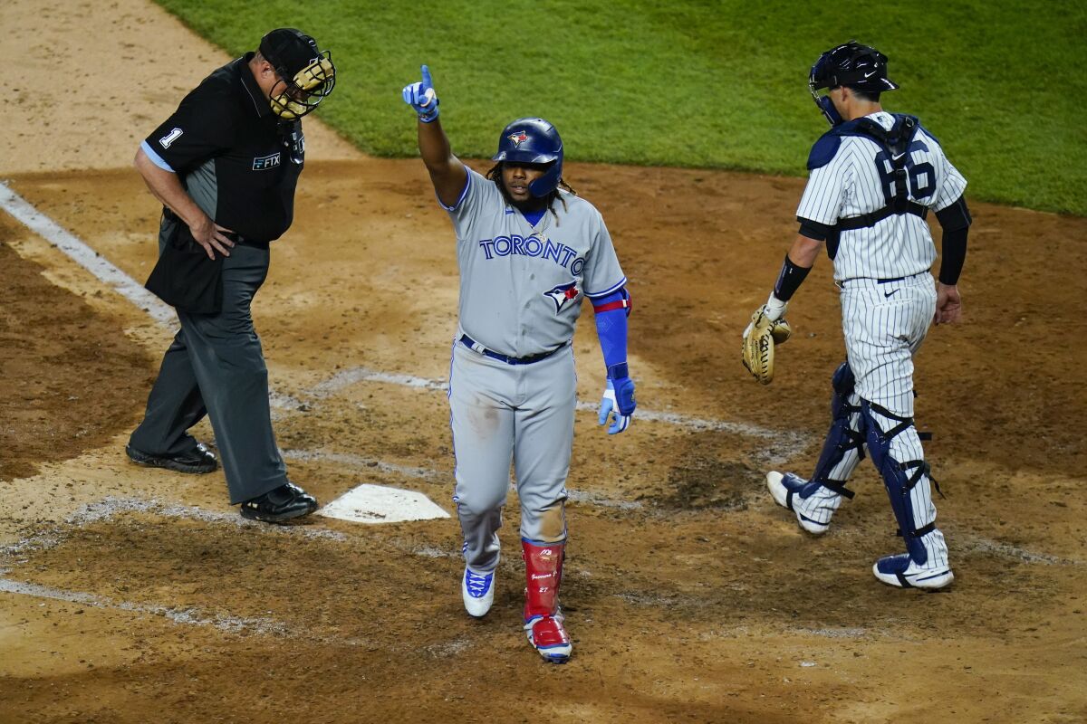 Toronto Blue Jays' Vladimir Guerrero Jr., center, gestures to fans after reaching home plate on a home run, next to New York Yankees catcher Kyle Higashioka during the eighth inning of a baseball game Wednesday, April 13, 2022, in New York. (AP Photo/Frank Franklin II)