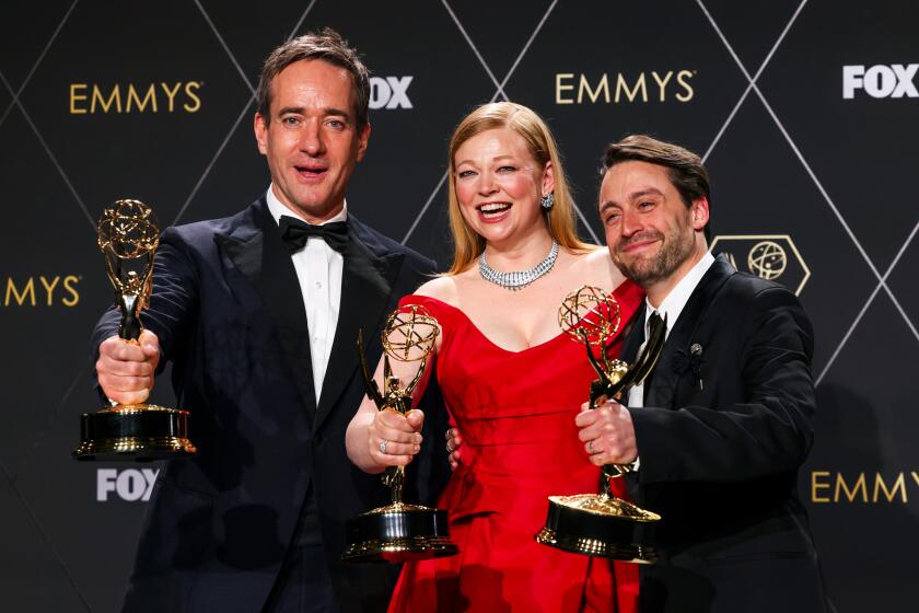 Three actors hold awards and smile for the camera.