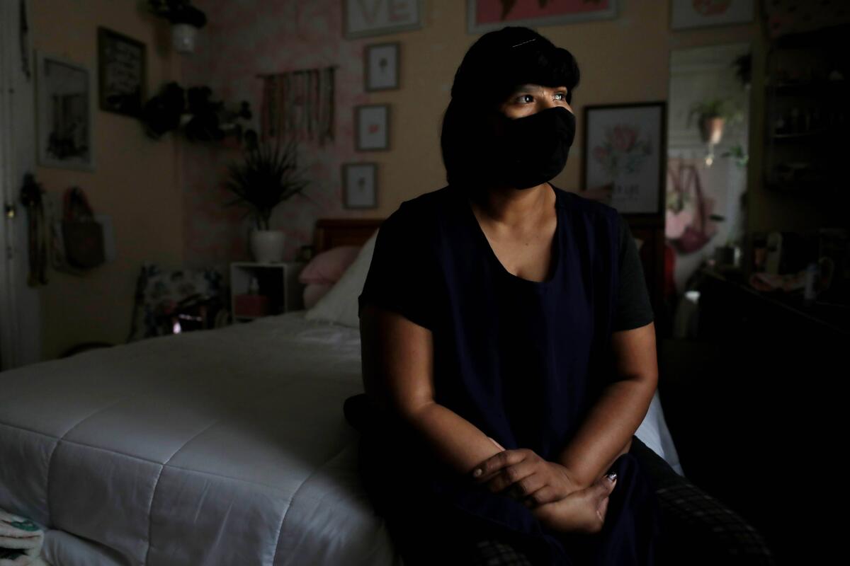 Victoria Galindo Lopez, a pandemic essential worker, sits on her bed with a mask on