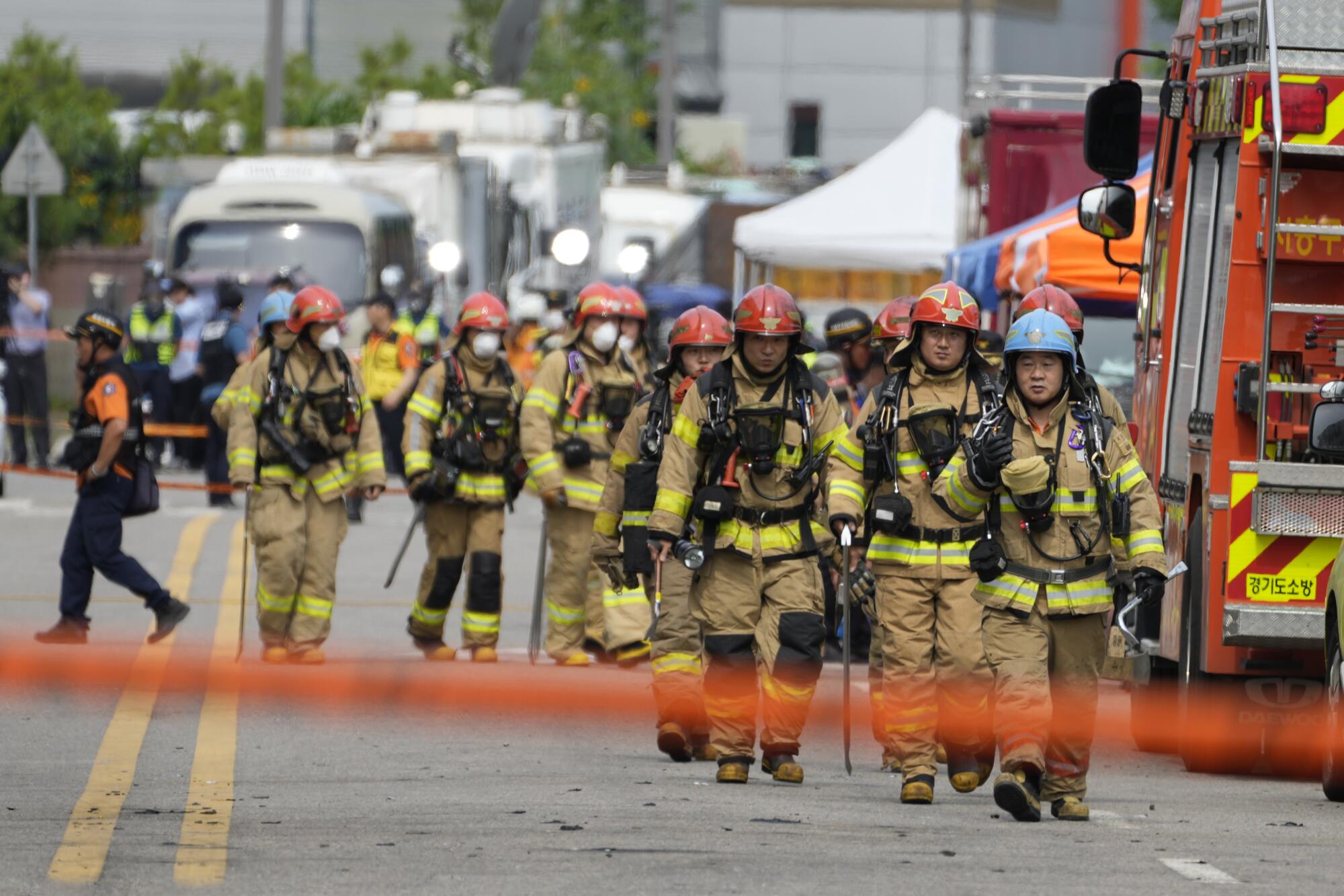 A line of firefighters in protective gear moves toward the camera.