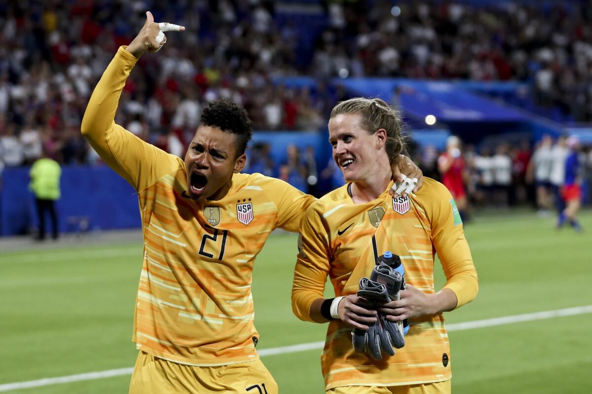 U.S. goalkeepers Adrianna Franch raises a pointer finger and Alyssa Naeher smiles on the field