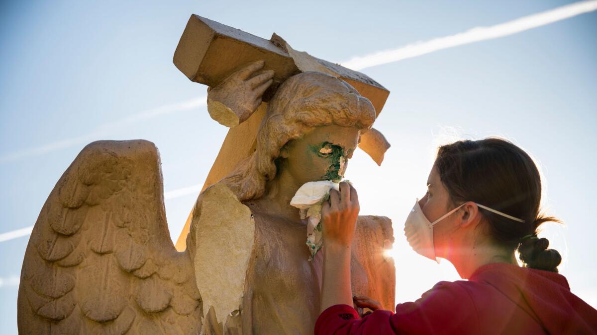 Evelyn Askew, 19, cleans an angel statue that was damaged and spray-painted with graffiti in front of Church of the Angels in Pasadena.