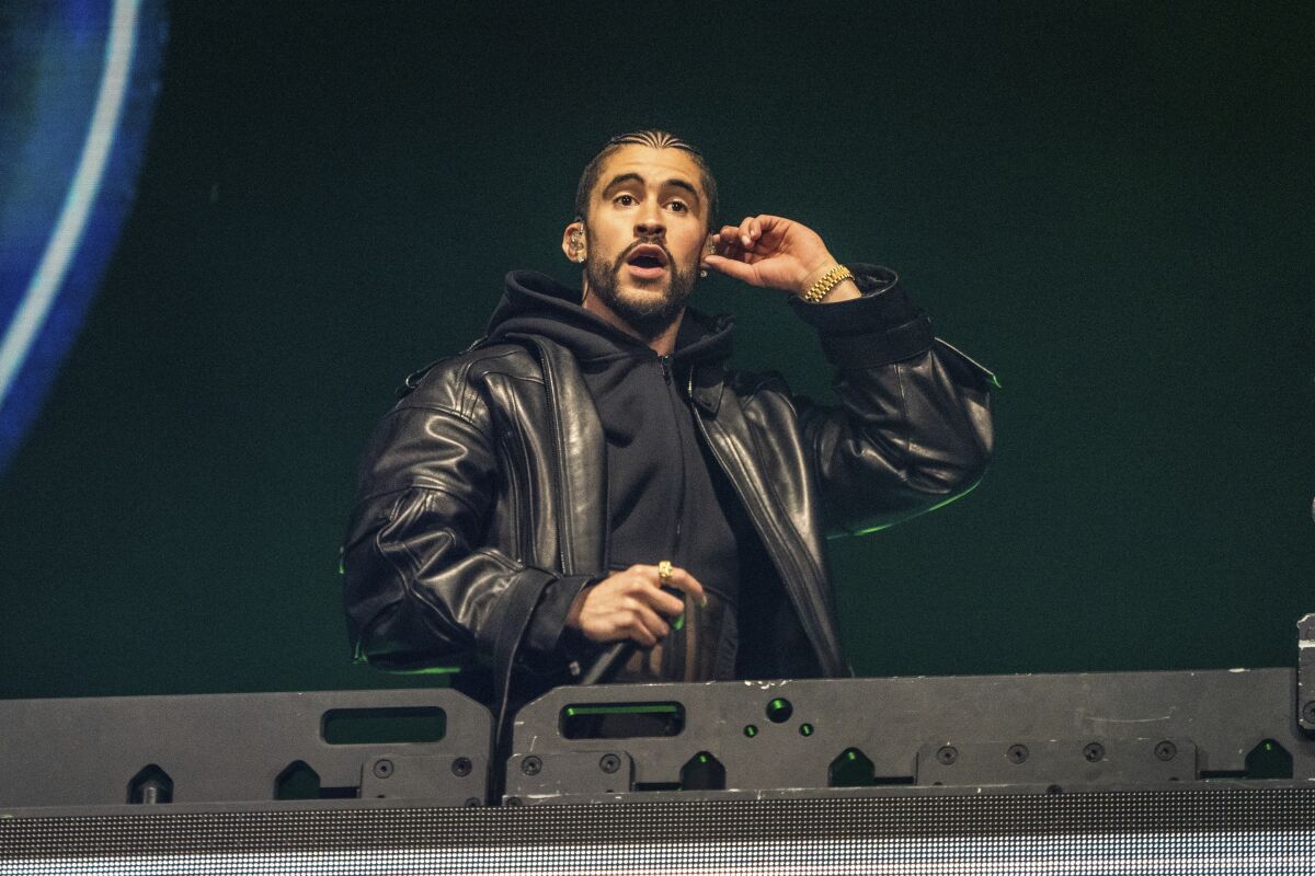 Bad Bunny adjusts his earpiece and holds a microphone while performing on a stage