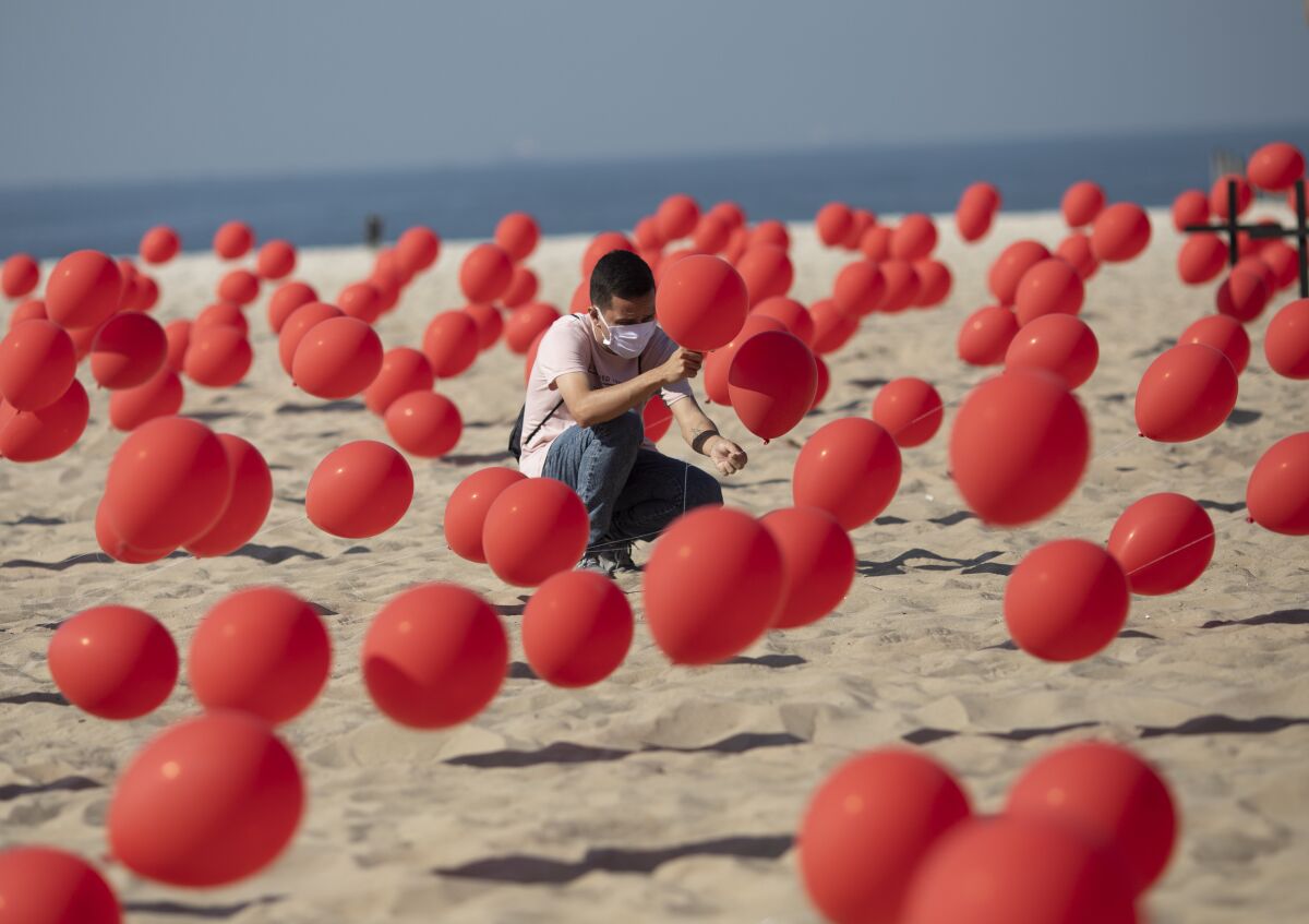 A man helps to place red balloons in the sand on Copacabana beach in a demonstration organized by Rio de Paz to honor the victims of COVID-19, as the country heads to a milestone of 100,000 new coronavirus related deaths, in Rio de Janeiro, Brazil, Saturday, Aug. 8, 2020. (AP Photo/Mario Lobao)